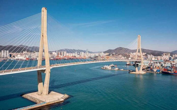 shutterstock_2265378171 Cable-stayed bridge spanning a harbor with city skyline and mountains