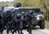 Tactical police team advances from armored vehicle with shields and rifles