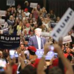 man at podium addressing a large crowd at a rally