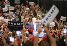 man at podium addressing a large crowd at a rally