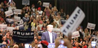 man at podium addressing a large crowd at a rally