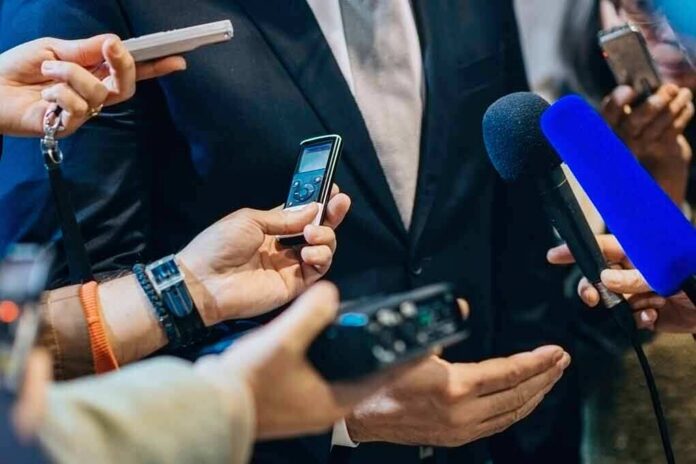businessperson in suit surrounded by microphones and recorders
