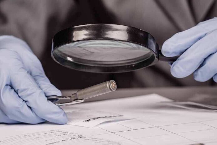 Gloved hands examine bullet casing with magnifying glass