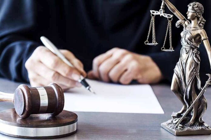 shutterstock_565403533 Judge writing at desk with gavel and Lady Justice statue