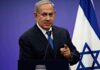 October 7 Could Decide Netanyahu’s Political Fate man in suit speaking at a podium with an Israeli flag