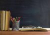 Books and pencils on a desk in front of a chalkboard
