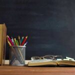 Books and pencils on a desk in front of a chalkboard