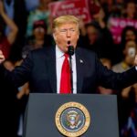 Donald Trump speaking at a rally podium with arms raised