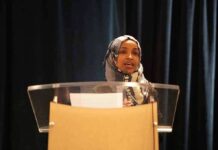 Ilhan Omar’s Home RAIDED Woman in hijab speaking at a podium