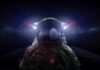 astronaut in space suit facing moon with helmet lights