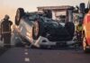 Overturned car on road with firefighters and ambulance
