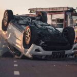 Overturned car on road with firefighters and ambulance