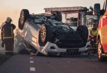 Overturned car on road with firefighters and ambulance