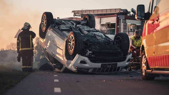 Overturned car on road with firefighters and ambulance