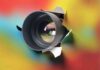 camera lens emerging through torn paper on colorful background