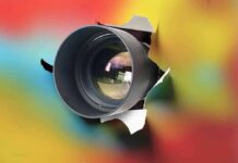 camera lens emerging through torn paper on colorful background