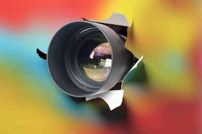 camera lens emerging through torn paper on colorful background