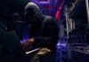 Hooded person using a laptop in a dark server room