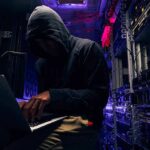 Hooded person using a laptop in a dark server room