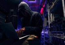 Hooded person using a laptop in a dark server room