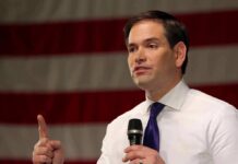 Rubio Calls Amnesty International a ‘FRAUD’ man speaking with microphone in front of an American flag